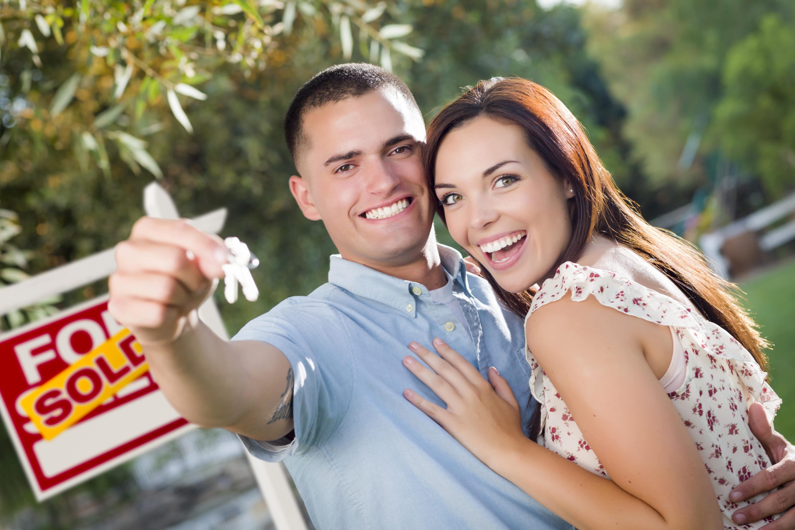 Mixed Race Excited Military Couple with New House Keys and Sold Real Estate Sign Outside