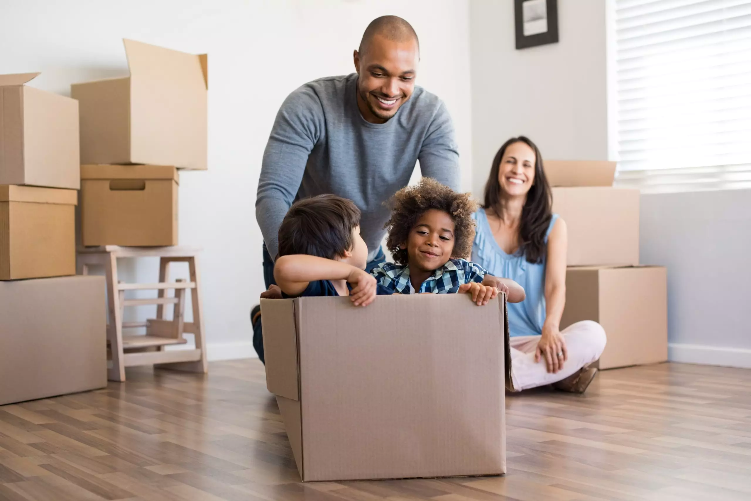 Happy african american father playing with children sitting in carton box at new home